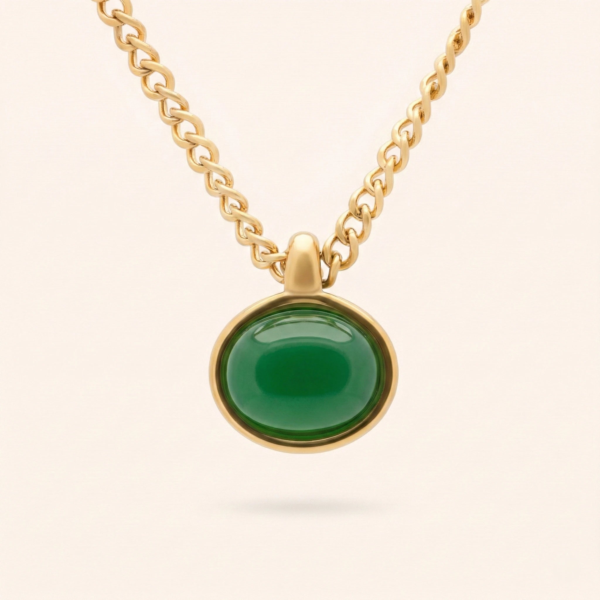 Gold necklace with a green pendant on a light beige background